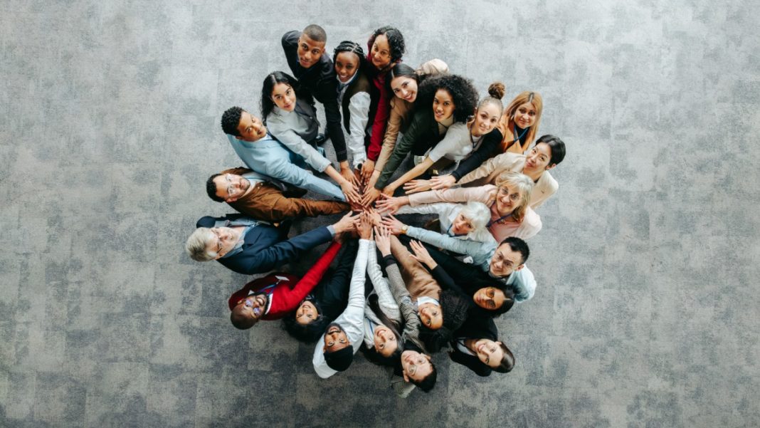 Many people putting their hands in the middle of a group, indicating inclusivity