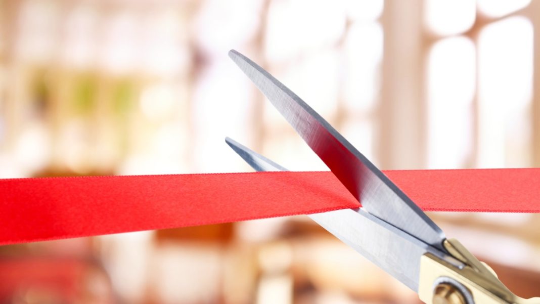 Close up on scissors cutting through a red opening ribbon