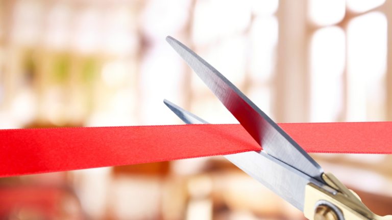 Close up on scissors cutting through a red opening ribbon