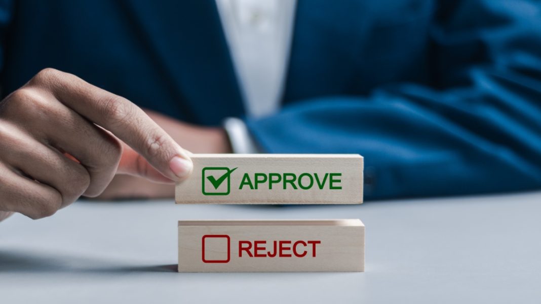 A wooden block with the word approve is held by a businessman