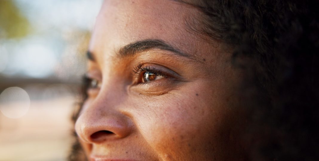 Rosto de mulher de lado, sorrindo, com foco nos olhos